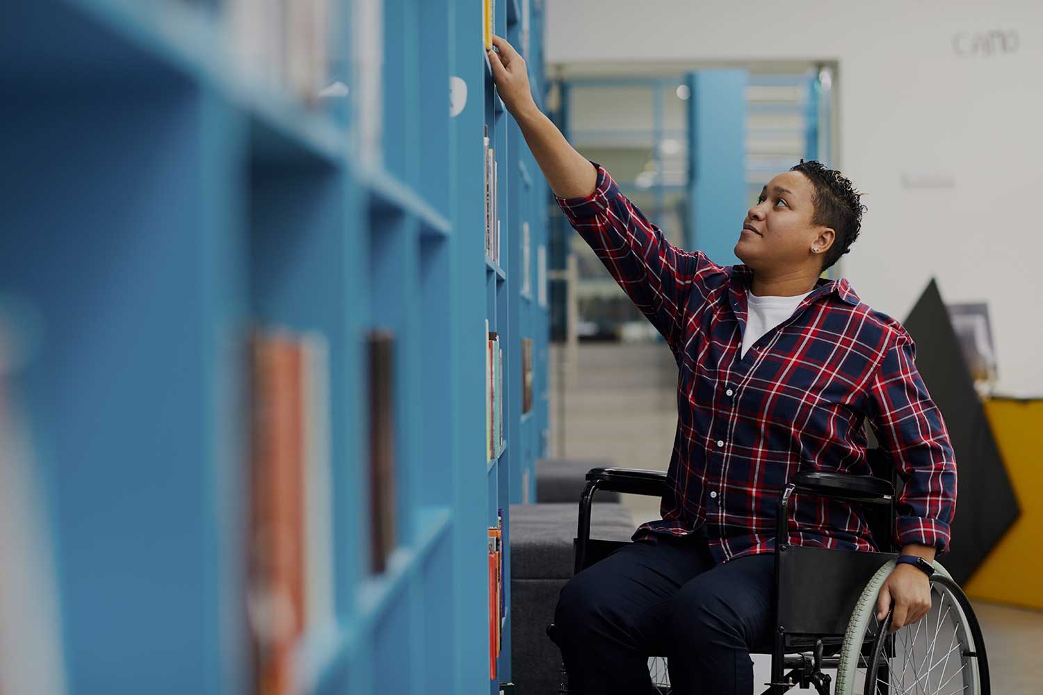 A student using a wheelchair reaches for a library book